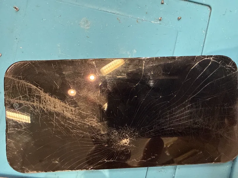 An iPhone with a badly cracked screen on a blue repair mat