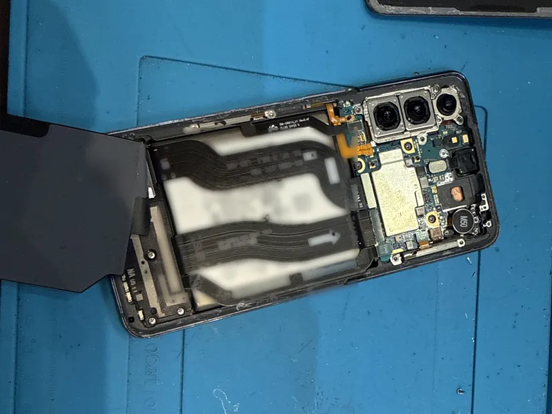 A Samsung Galaxy phone opened up on a blue repair mat, with its battery, circuit board and cameras visible and screws laid out beside it